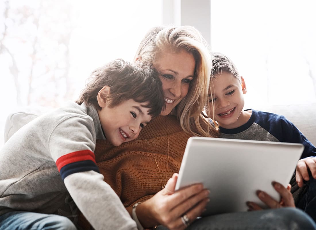 Blog - Portrait of a Cheerful Mother Sitting with her Two Young Boys on the Sofa Having Fun Watching Videos on a Tablet Together