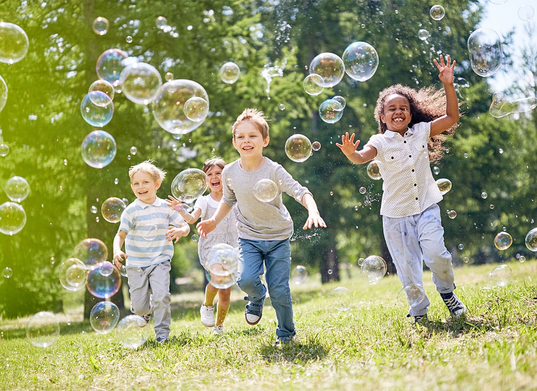Child Life Insurance - Happy Diverse Children Running on the Green Grass Playing with Bubbles
