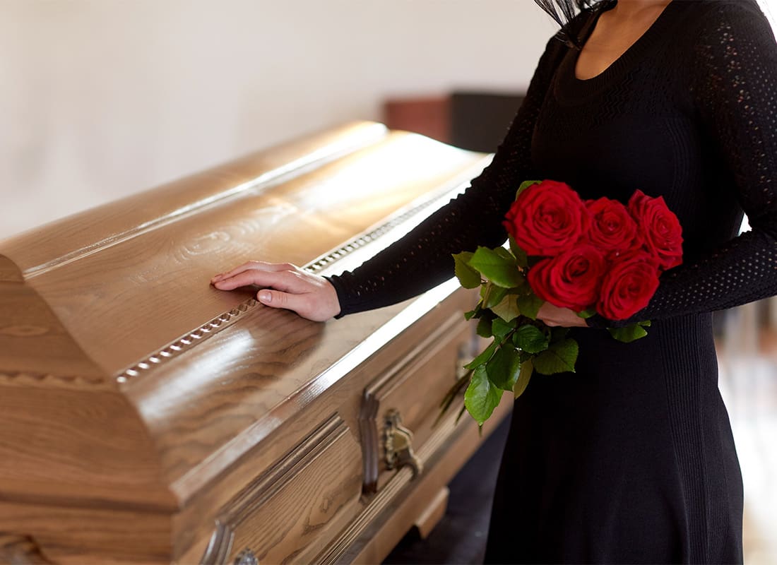Final Expense Insurance - View of a Woman in Black Holding Red Roses with the Other Hand on a Wooden Casket