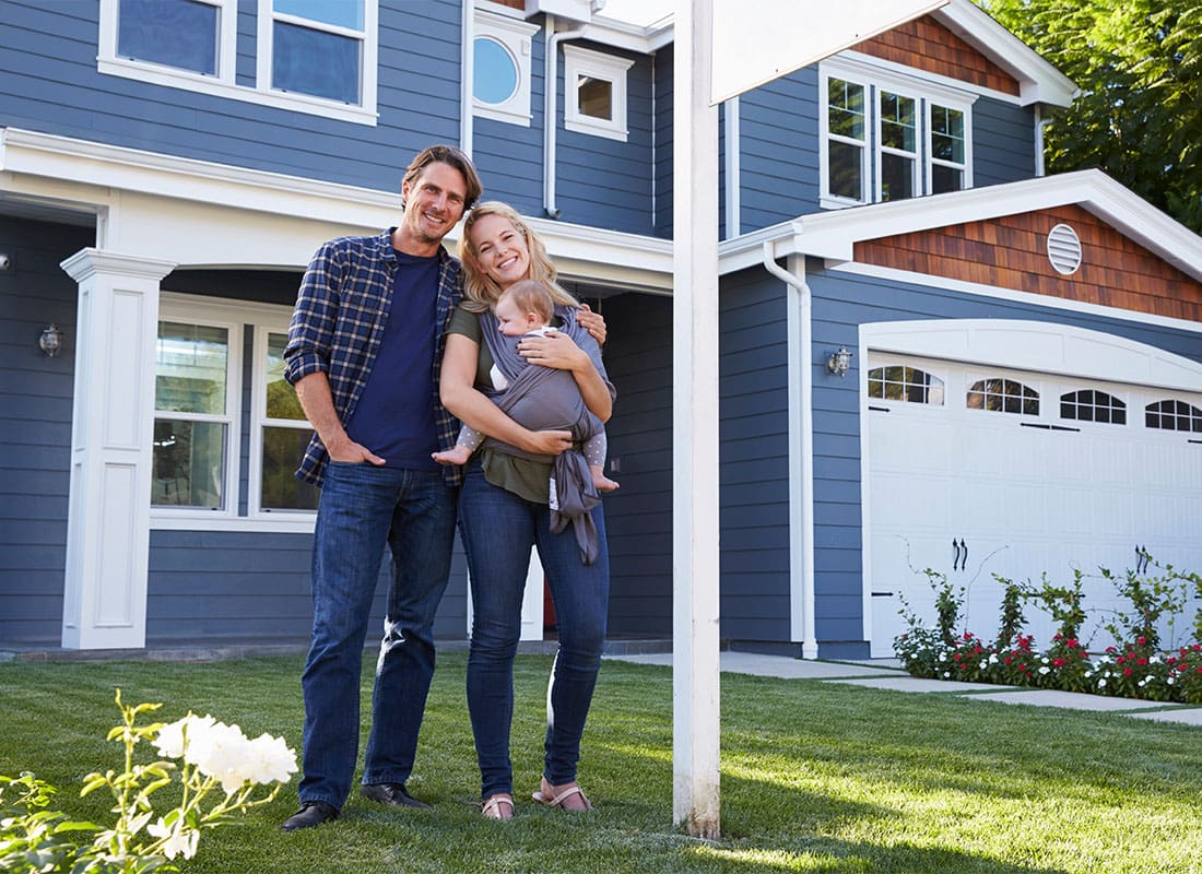 Personal Insurance - Portrait of a Smiling Young Couple with a Baby Standing Outside Their New Two Story Home
