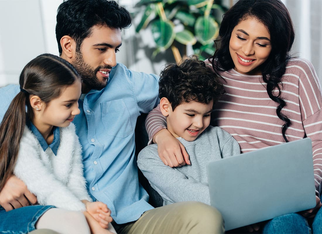 Refer Us - Portrait of Parents and Their Son and Daughter Spending Time Together in the Living Room While Using a Laptop